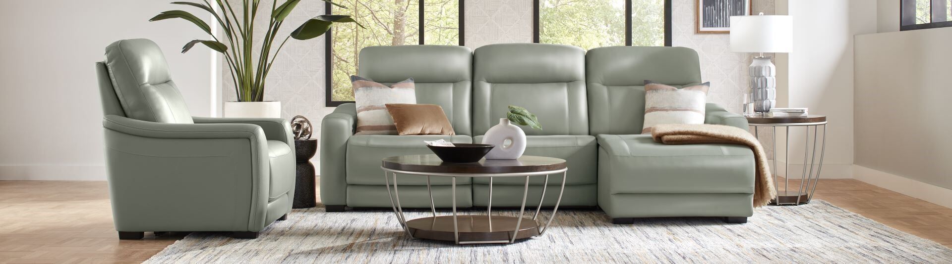 A light green leather sofa and recliner with a coffee table and rug.
