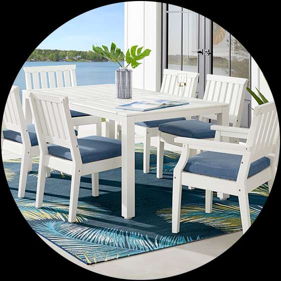 White outdoor dining set with blue cushions on a blue patterned rug.
