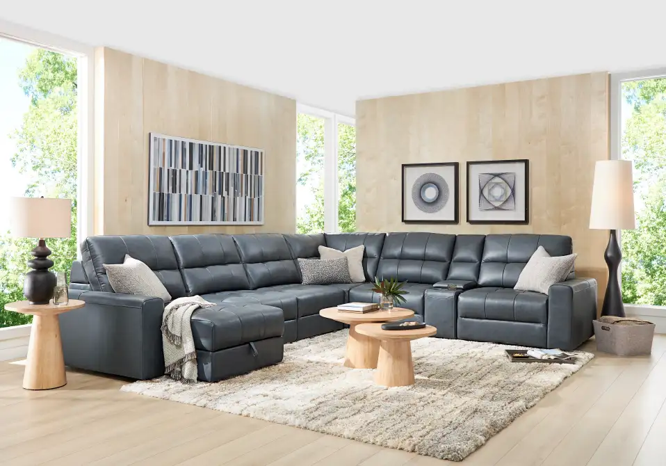 A large, gray sectional sofa with a matching ottoman, on a shaggy rug, in a modern living room.
