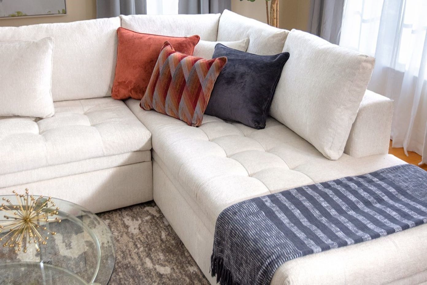 White sectional sofa with orange and gray pillows and a blue throw blanket.
