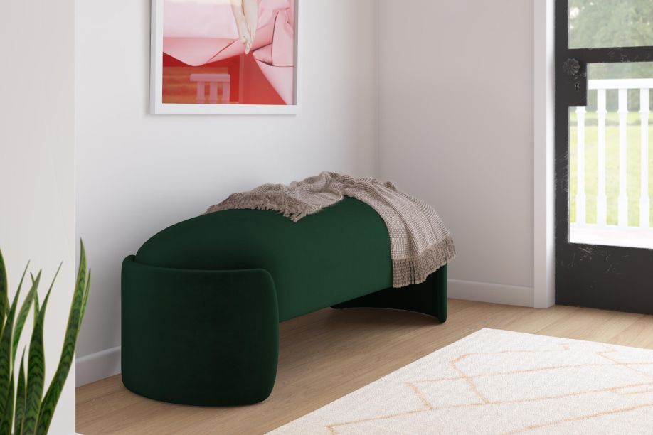 A dark green curved bench with a blanket on top, next to a white rug.
