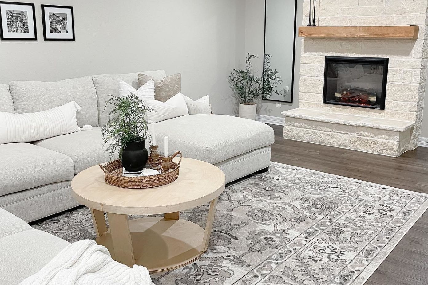 A living room with a light gray sectional sofa, a round coffee table, and a stone fireplace.
