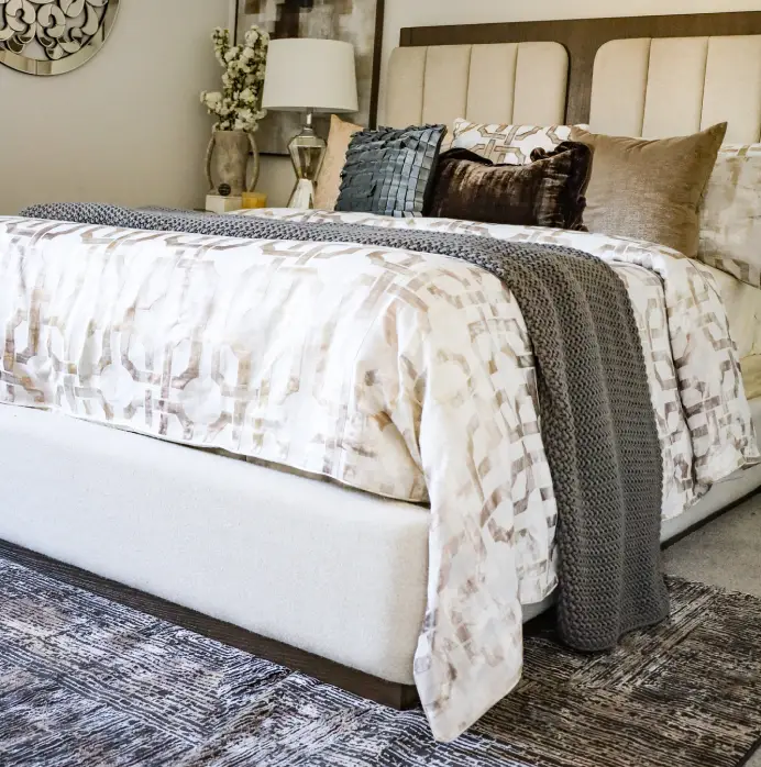 A modern bedroom featuring a bed with a geometric patterned duvet, a chunky grey knit throw, and decorative pillows.