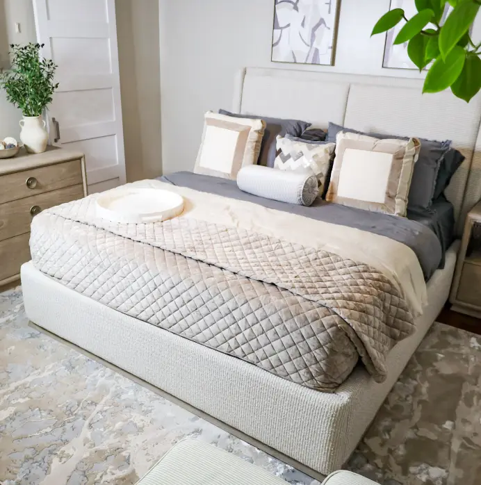 A modern bedroom featuring a beige upholstered bed with a quilted coverlet, grey bedding, and decorative pillows.