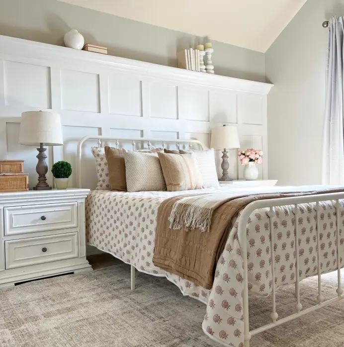 A cozy bedroom featuring a white metal bed frame, floral bedding, a tan throw blanket, and a white paneled headboard wall.