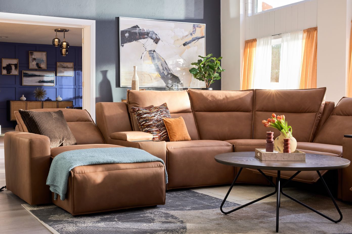 Brown leather sectional sofa with a blue throw blanket and a round coffee table.
