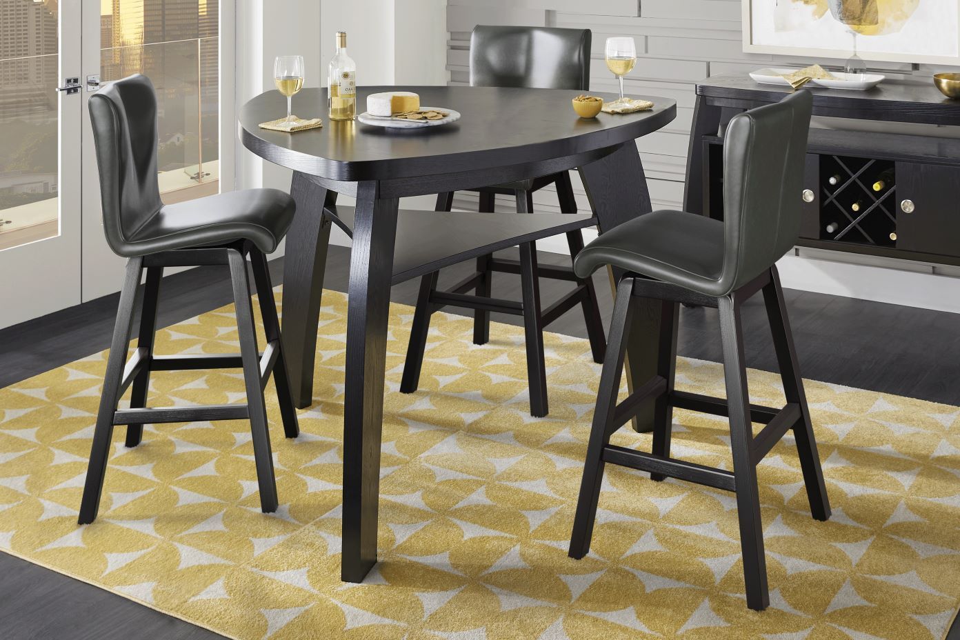 A black triangular table with matching bar stools on a yellow patterned rug.
