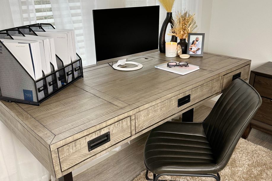 A wooden desk with a black monitor, a black chair, and decorative items.
