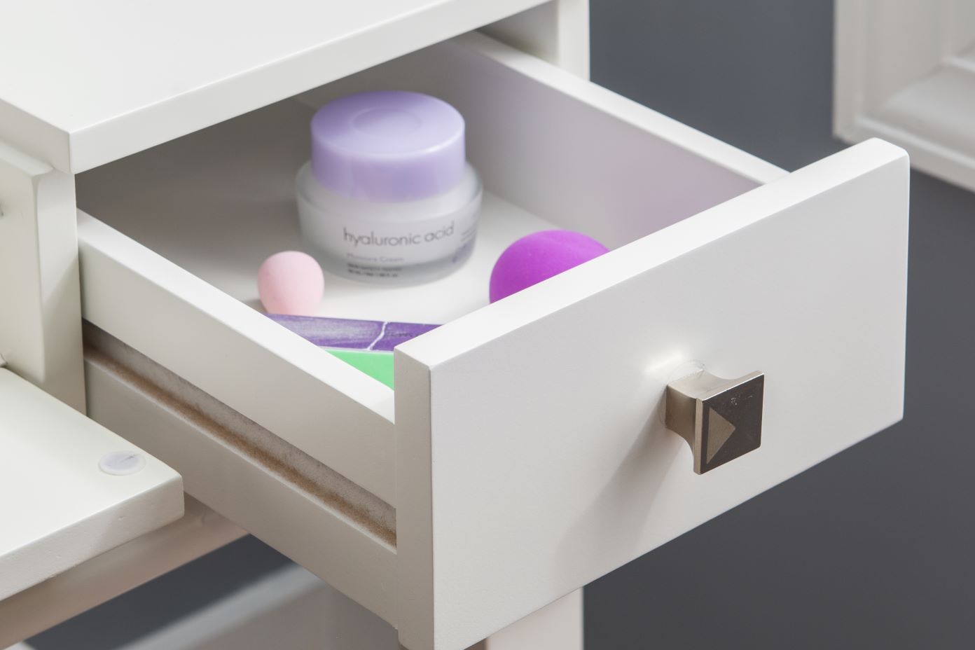 A white drawer with a silver knob, containing skincare products.
