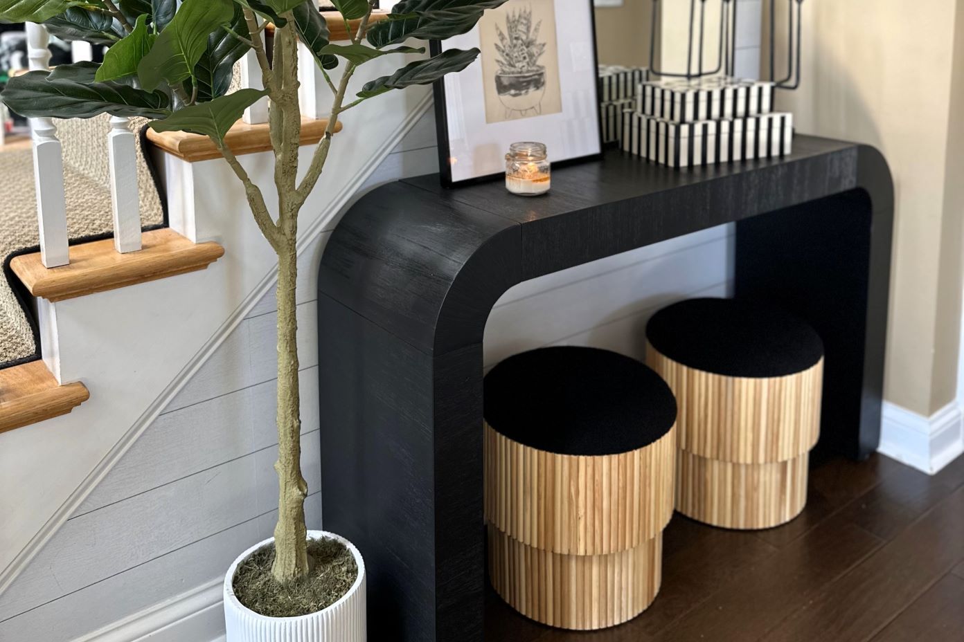 A black console table with two wooden stools, a potted plant, and decorative items.
