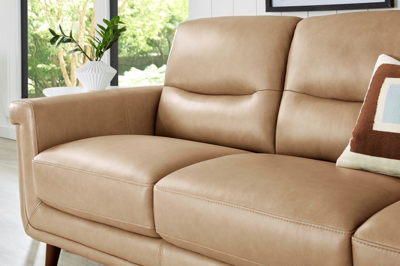 Tan leather sofa with a decorative pillow.
