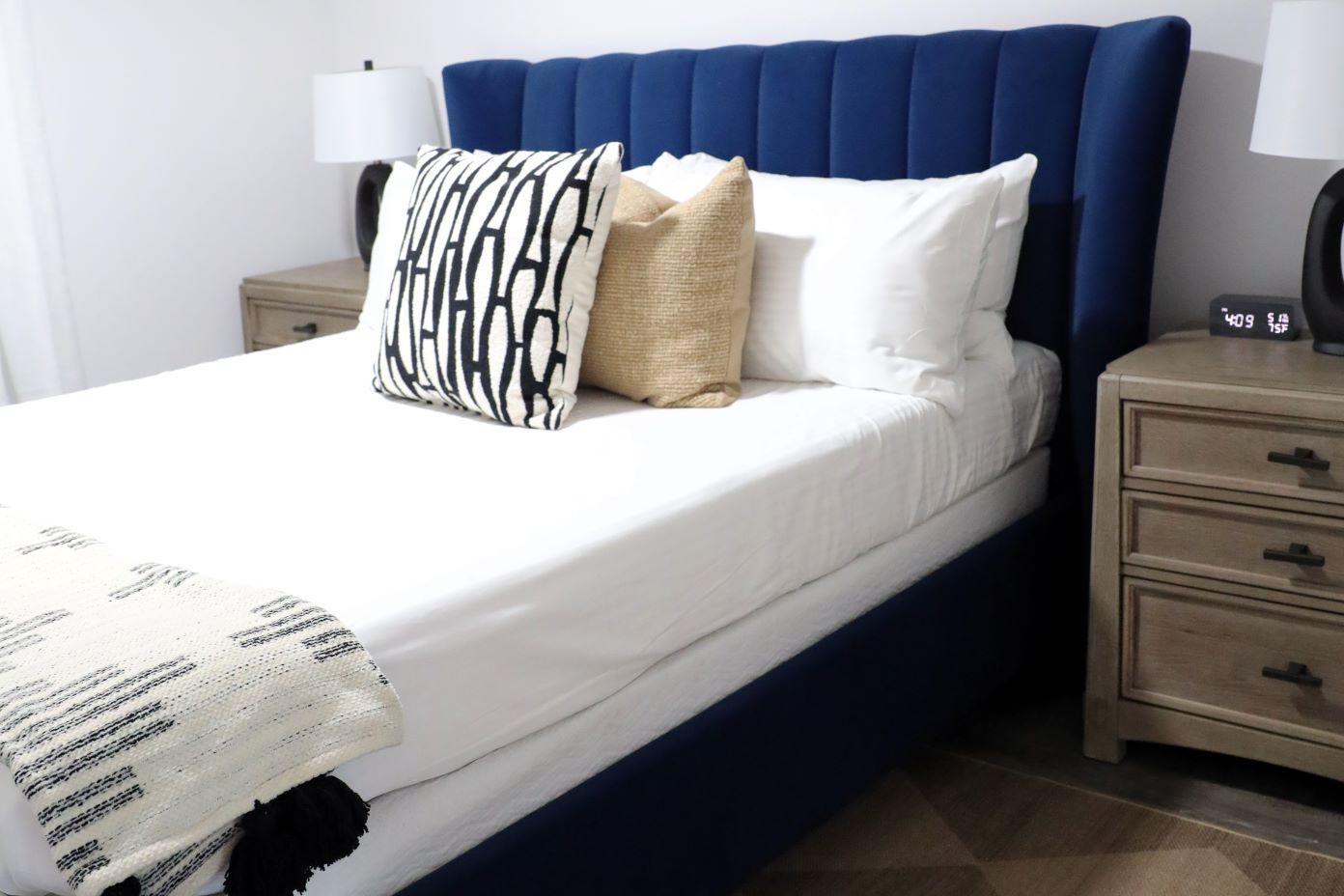 A bed with a blue headboard, white sheets, and decorative pillows.
