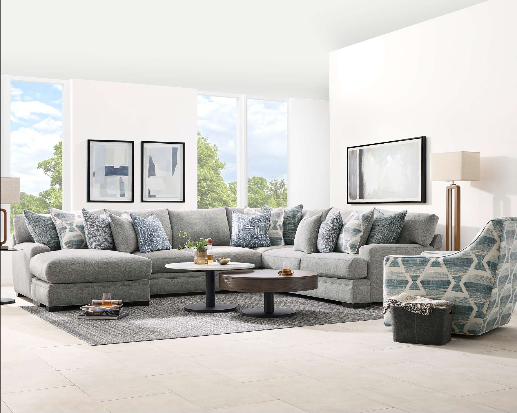 A gray sectional sofa with patterned pillows, two coffee tables, and a patterned armchair.

