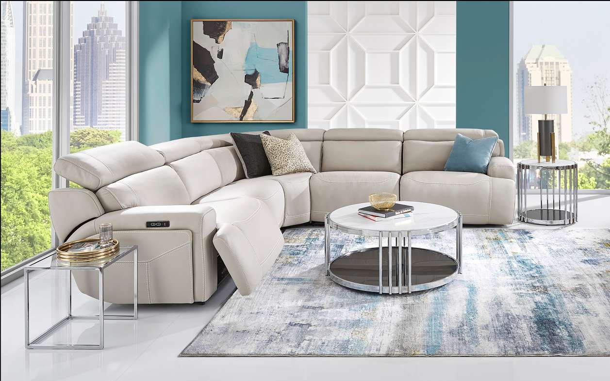 Cream-colored sectional sofa in a modern living room with a round coffee table and a patterned rug.
