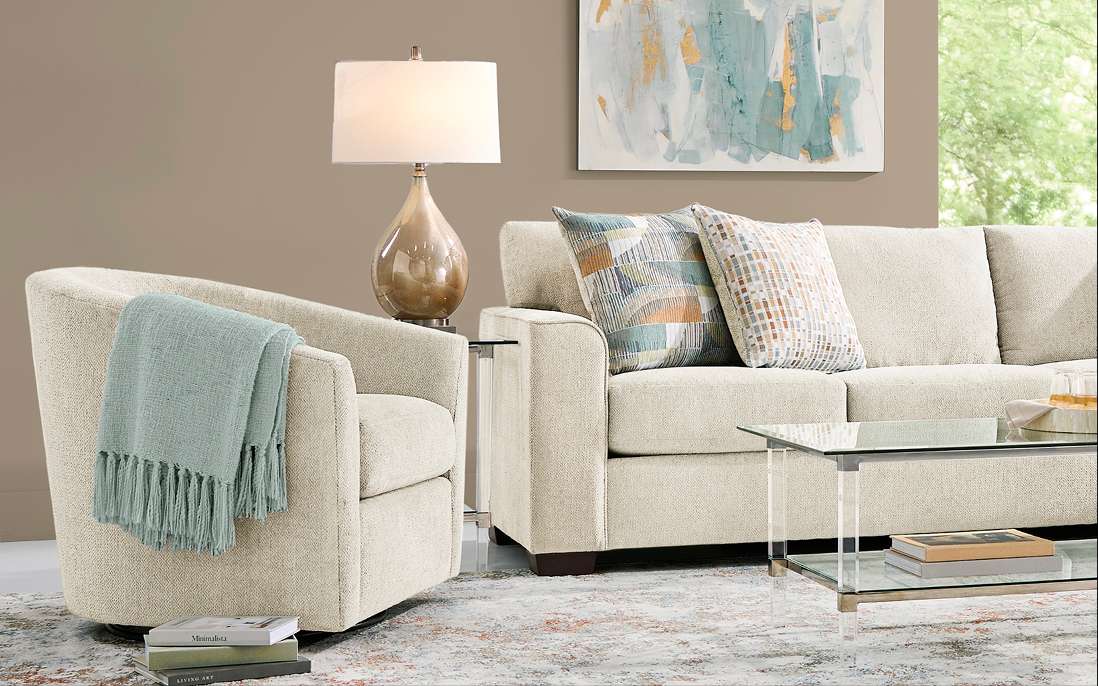 A living room with a beige sofa, armchair, and glass coffee table.

