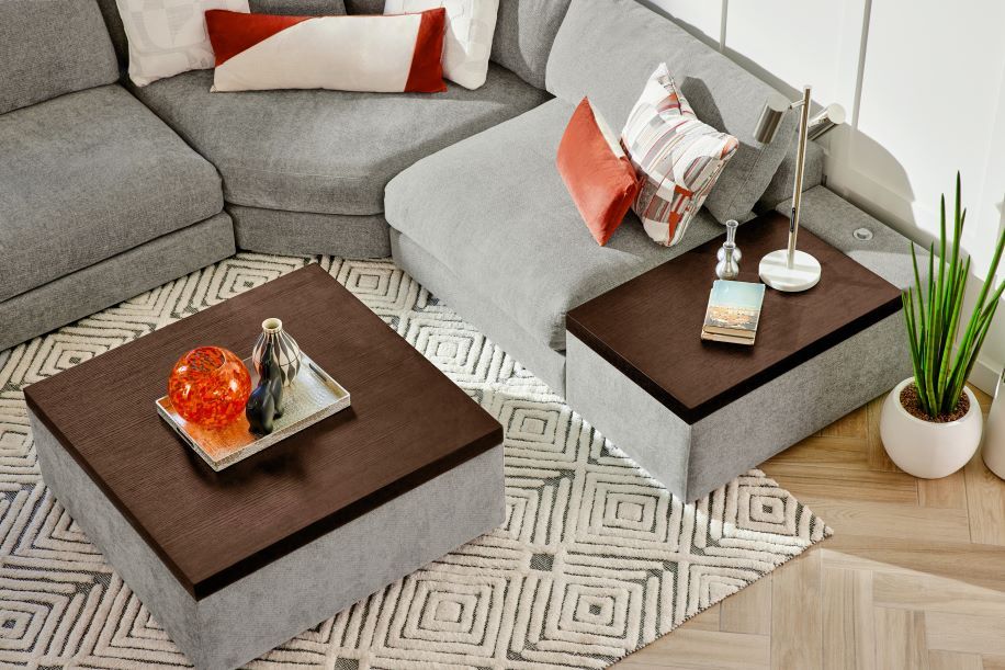 A modern living room with a gray sectional sofa, two dark brown coffee tables, and a patterned rug.
