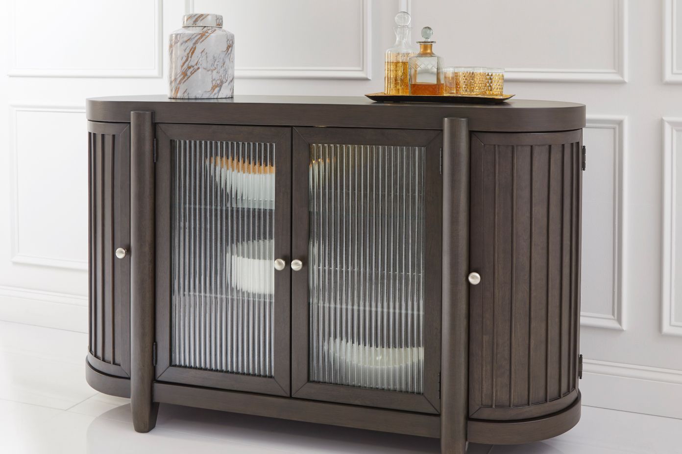 Dark brown cabinet with glass doors and decorative items on top.
