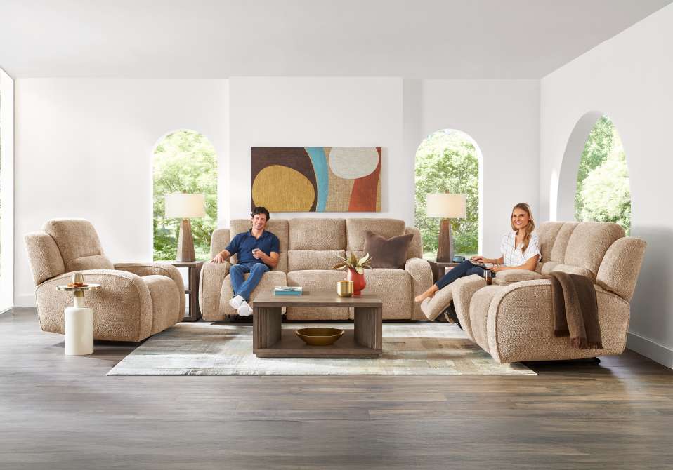 A living room with a sofa, two recliners, and a coffee table. A man and a woman are relaxing.