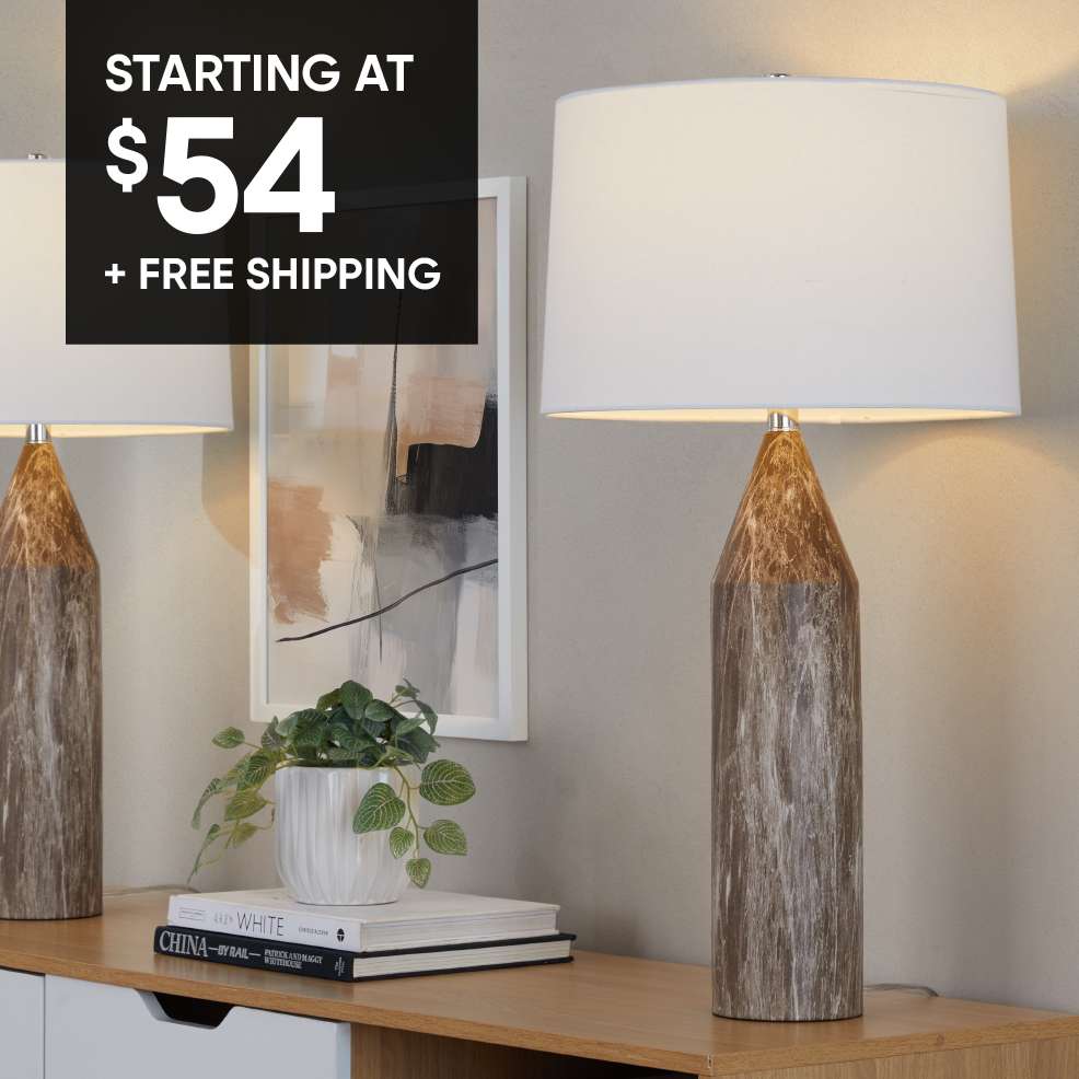STARTING AT $54 + FREE SHIPPING. Two lamps with white shades on a wooden surface.
