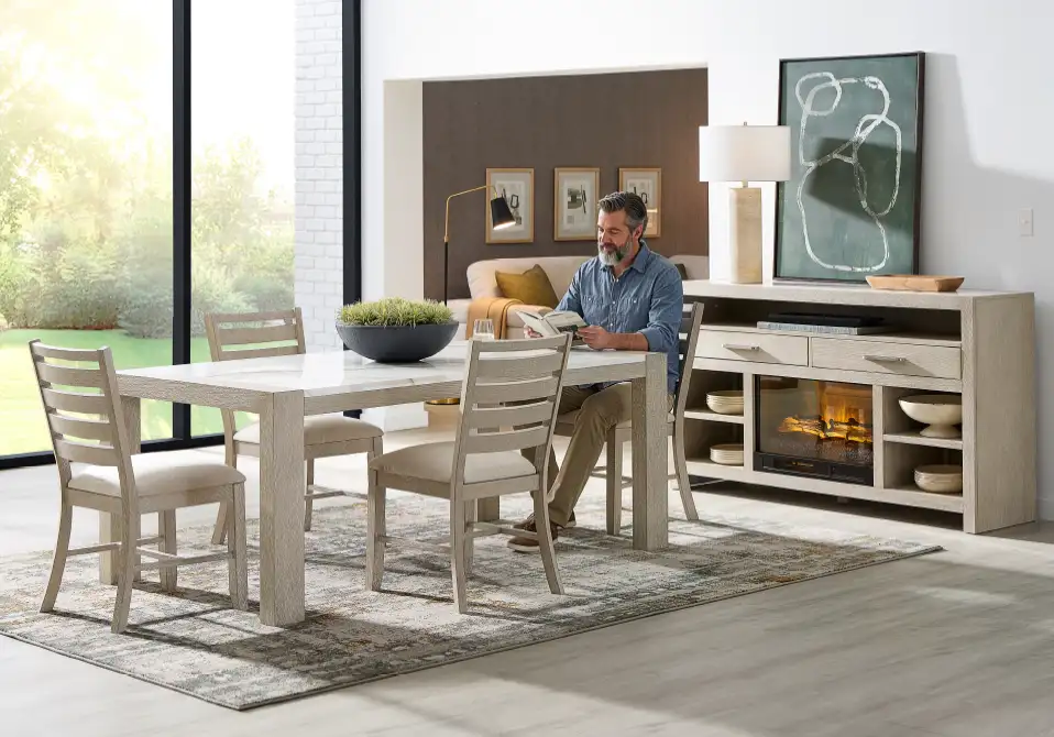A dining room with a table, chairs, and a man reading.