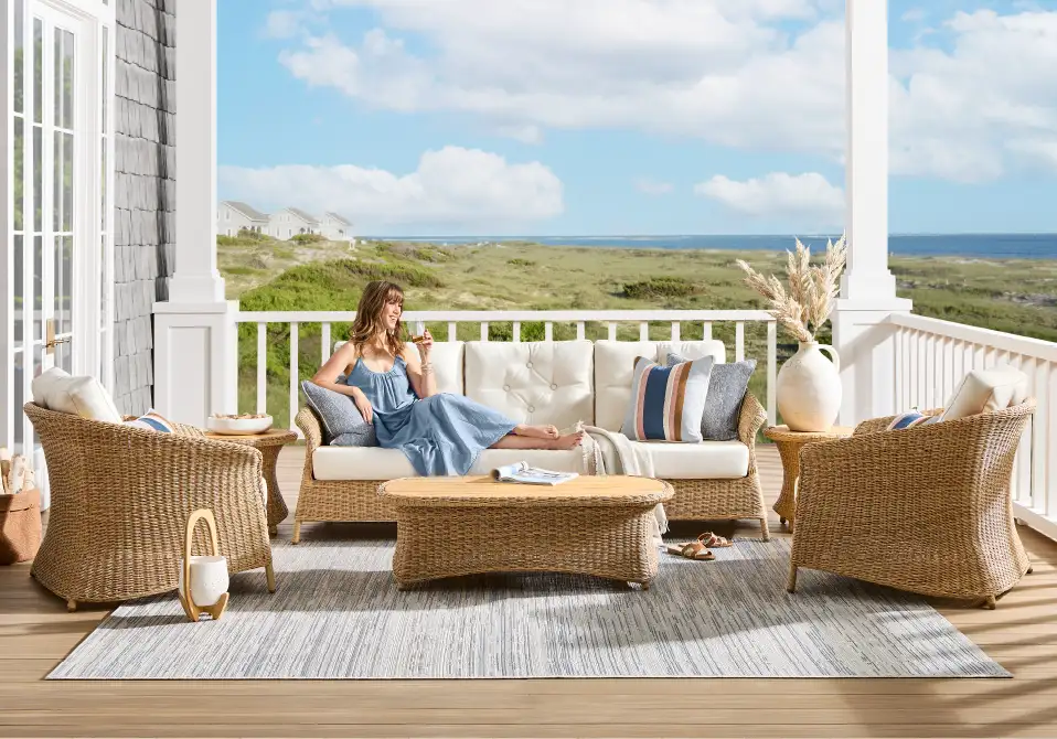 A woman relaxing on a wicker sofa on a porch overlooking the ocean.