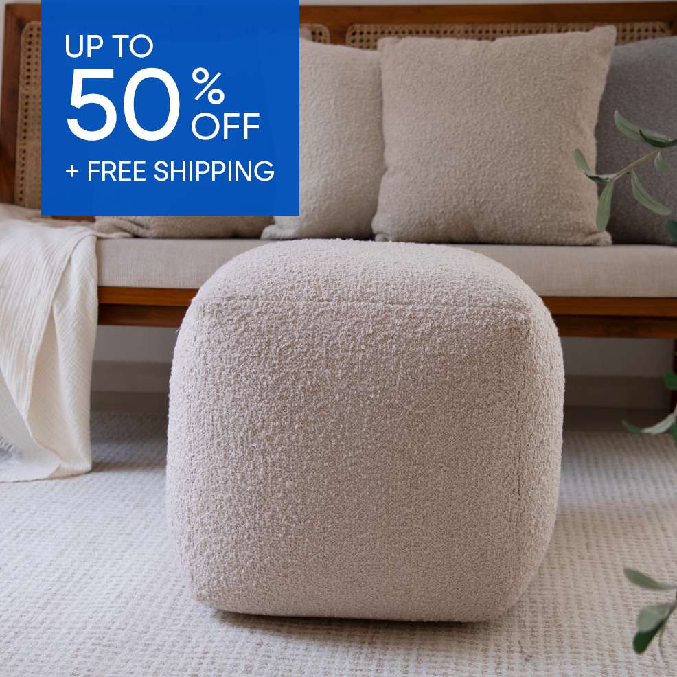 Up to 50% off + free shipping. A beige, square ottoman on a patterned rug.
