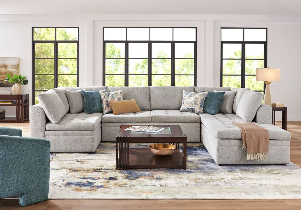 A large gray sectional sofa with decorative pillows, a coffee table, and a patterned rug.
