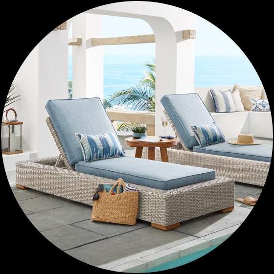 Two outdoor chaise lounges with blue cushions and pillows, next to a pool.
