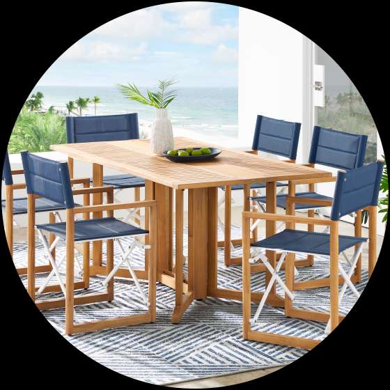 Outdoor dining set with a wooden table and blue director's chairs on a patterned rug.
