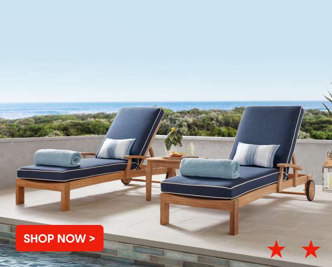 SHOP NOW > Two blue cushioned chaise lounges on a patio overlooking the ocean.
