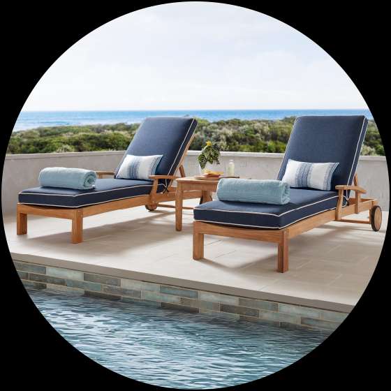 Two blue cushioned chaise lounges with towels and pillows by a pool.
