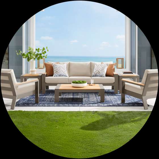 Outdoor patio furniture set with a sofa, two chairs, and a coffee table on a blue rug.
