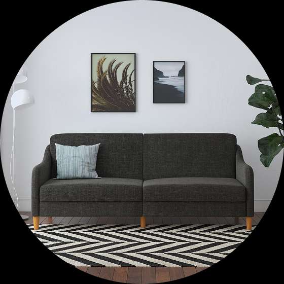 A dark gray sofa with a blue pillow, two framed pictures, and a black and white rug.
