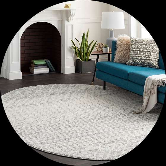 A round, light-colored rug with a geometric pattern in a living room with a blue sofa and fireplace.
