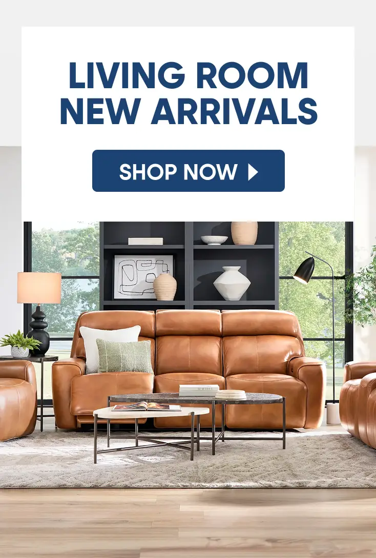 LIVING ROOM NEW ARRIVALS SHOP NOW. A tan leather reclining sofa in a modern living room with a coffee table and decor.