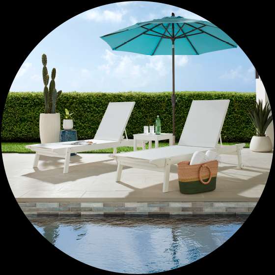 Two white chaise lounges with a blue umbrella by a pool.
