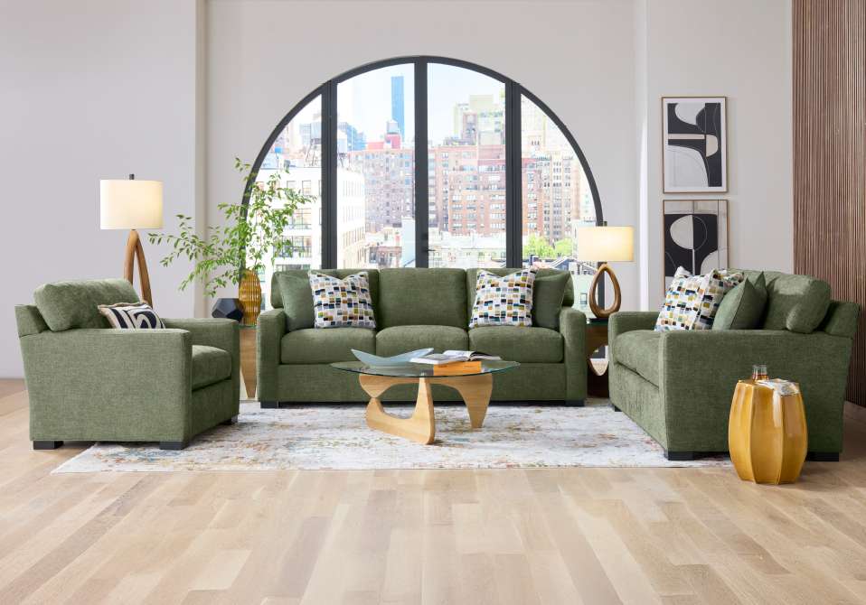 Green sofa and armchairs in a living room with a large arched window.
