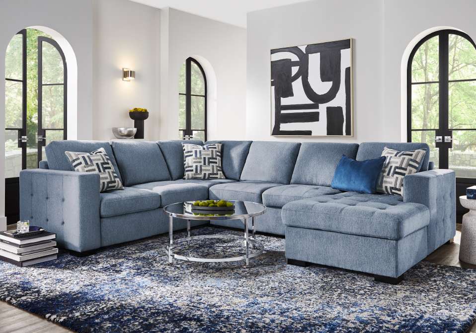 Blue sectional sofa with patterned pillows on a blue and white rug.
