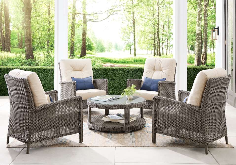 Four wicker armchairs arranged around a round coffee table on a patio.
