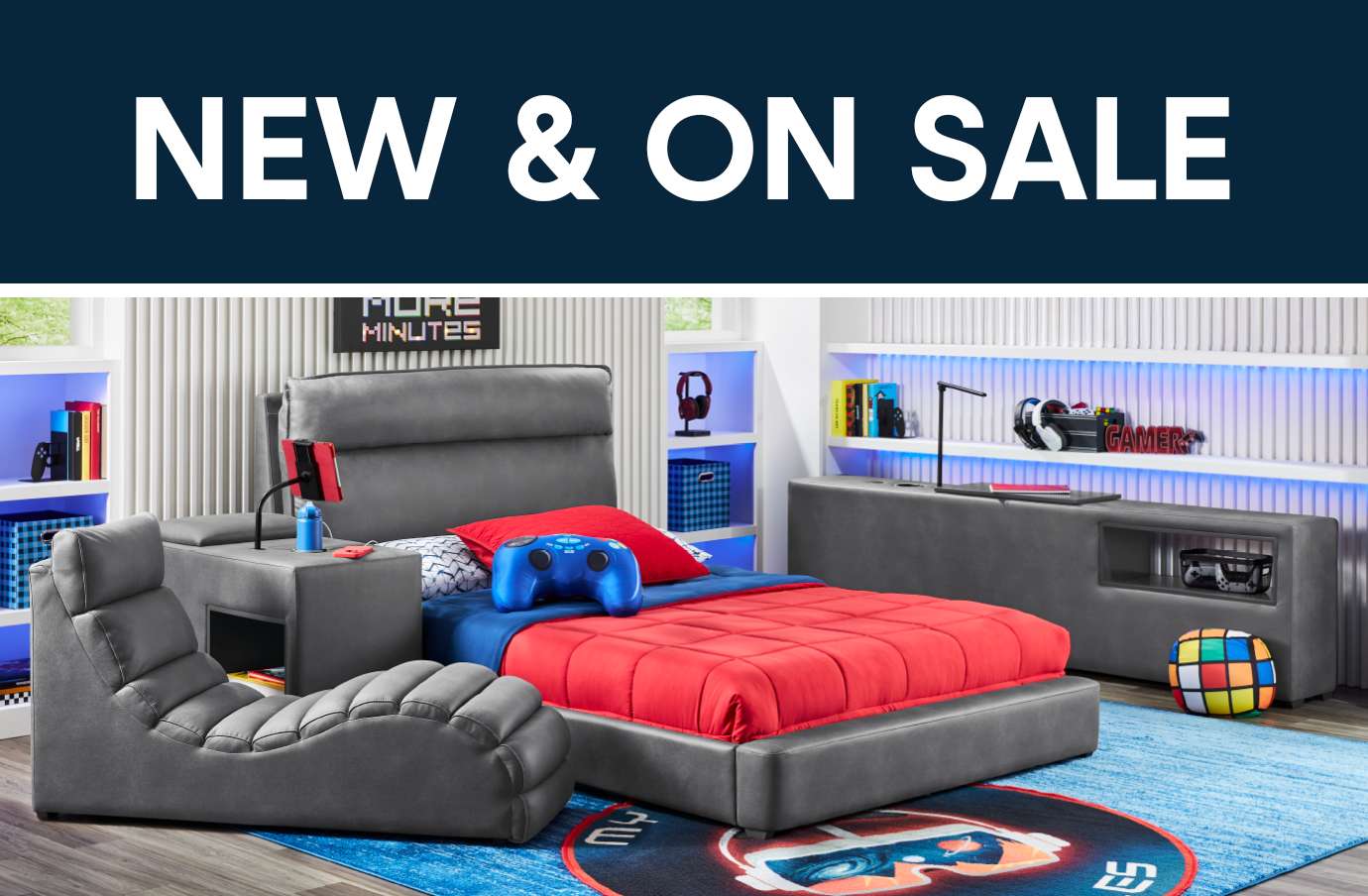NEW & ON SALE. A gray gaming bed with a red comforter, blue rug, and a gray chair.