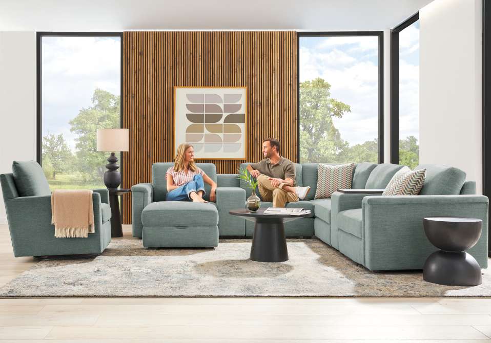 A living room with a sectional sofa, two people, and a rug.
