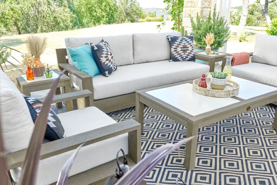Outdoor furniture set with a sofa, chairs, and coffee table on a patterned rug.
