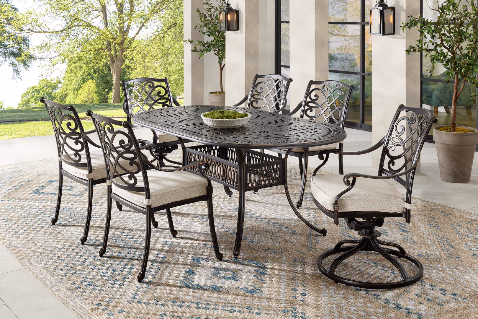 Outdoor dining set with an oval table and six chairs on a patterned rug.
