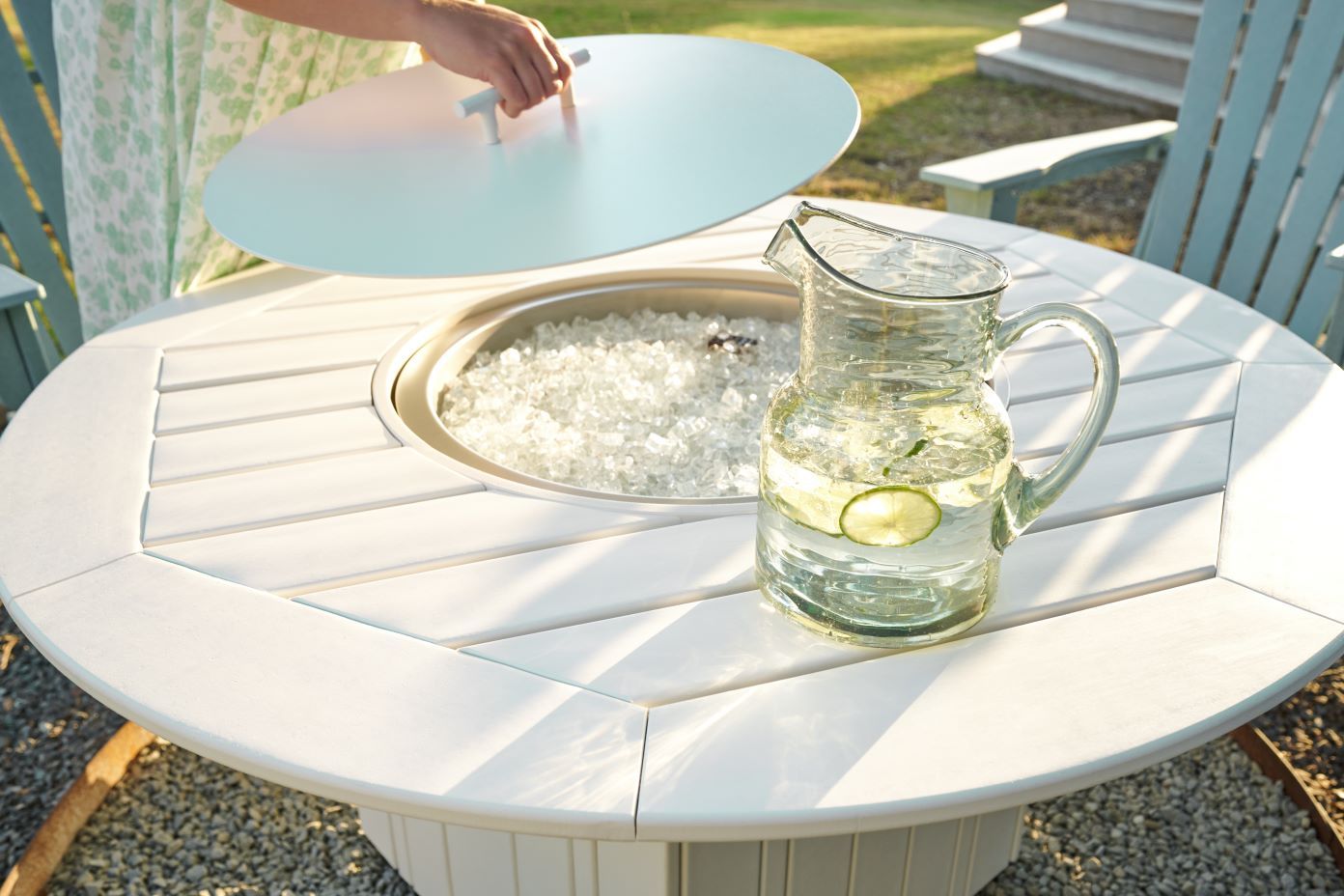 White outdoor fire pit table with ice and a pitcher of water with lime.
