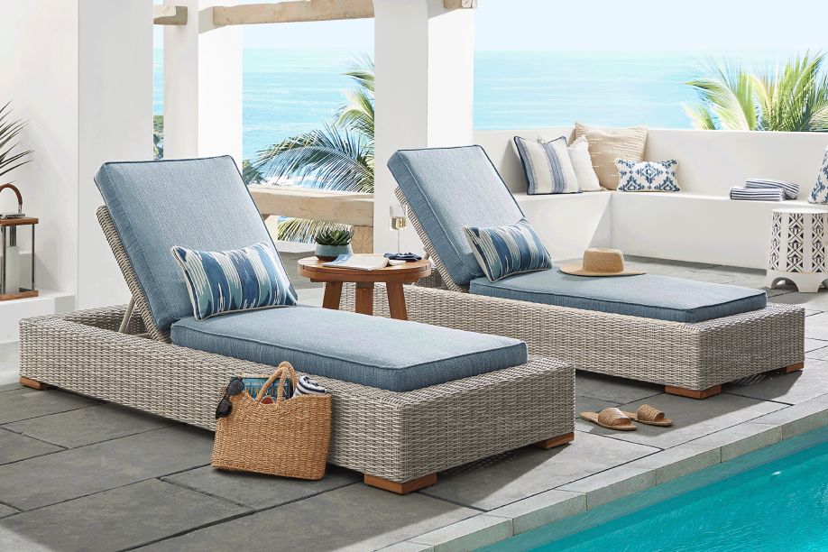 Two wicker chaise lounges with blue cushions and pillows by a pool.
