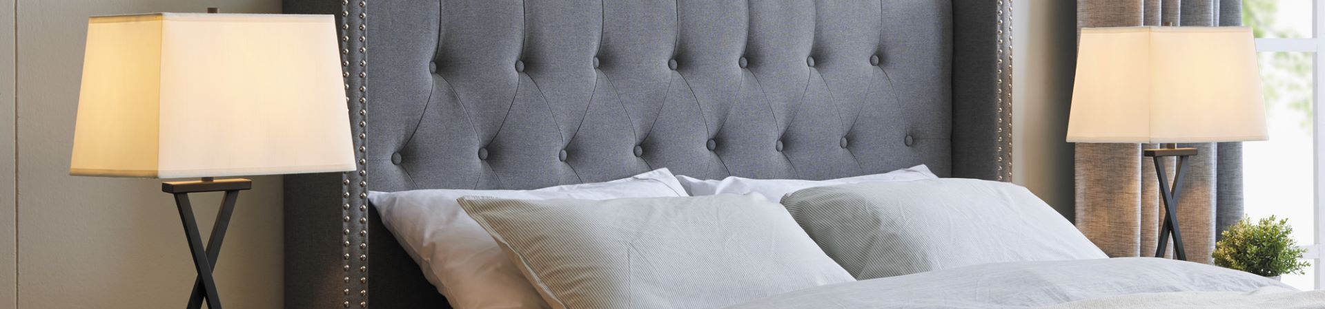 A gray tufted headboard with two lamps and pillows on a bed.