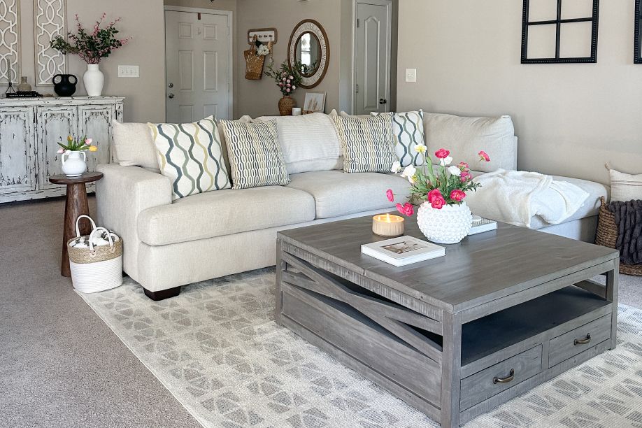 A living room with a beige sectional sofa, gray coffee table, and a patterned rug.
