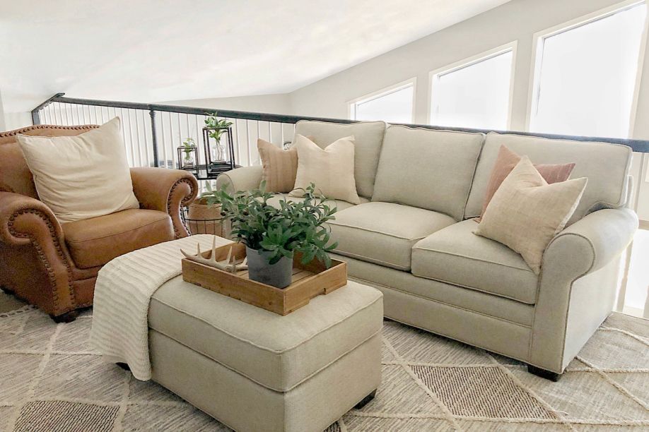 A living room with a brown leather armchair, a beige sofa, and an ottoman.
