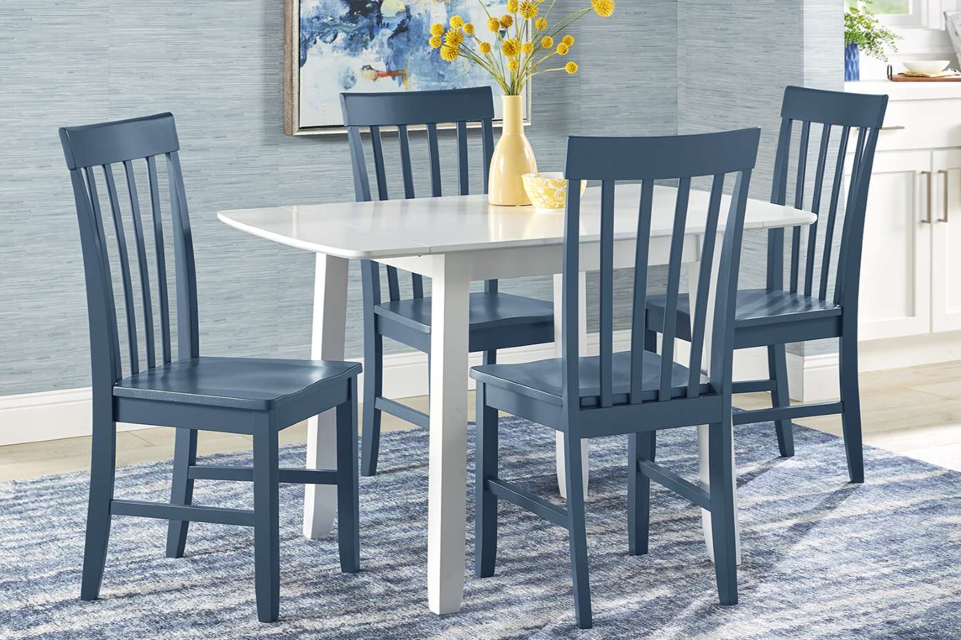 A dining table with four blue chairs, a vase of yellow flowers, and a blue rug.
