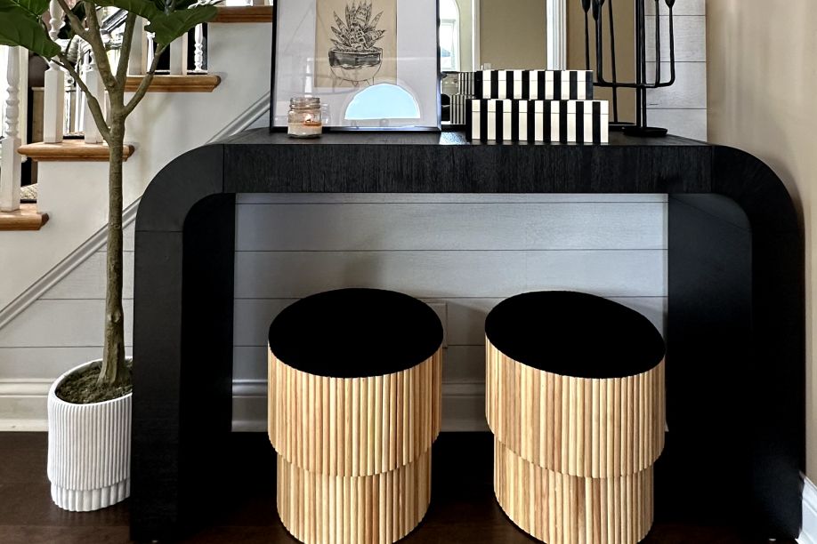 A black console table with two wooden stools. A plant and decorative items are on the table.
